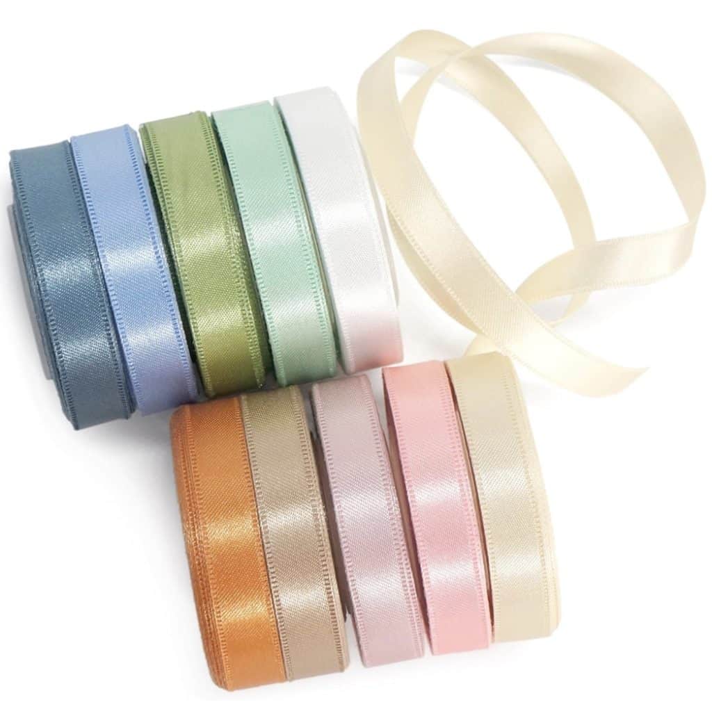 Eight rolls of satin ribbon in pastel colors—blue, green, white, beige, orange, pink, peach, and gold—are arranged on a white surface. Use them in craft projects or learn how to make suncatchers with a delicate beige ribbon unrolled at the top.